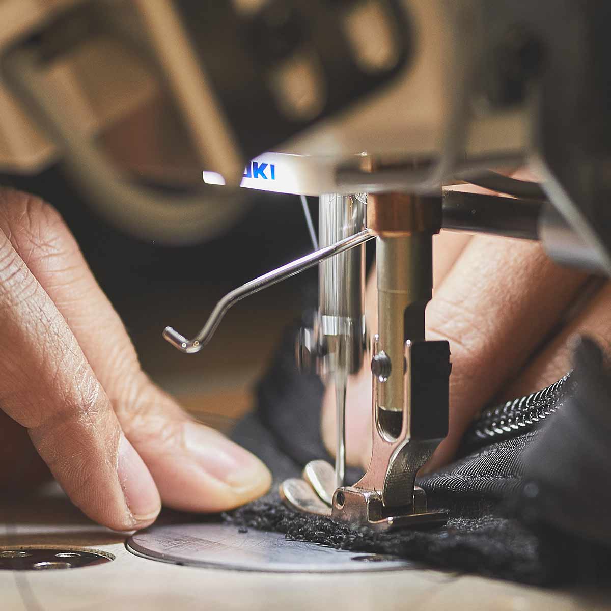 Close-up of hands guiding fabric under the needle of a sewing machine, focusing on stitching details as they perform a meticulous repair using the Scars Repair Form by GORUCK on a damaged product.