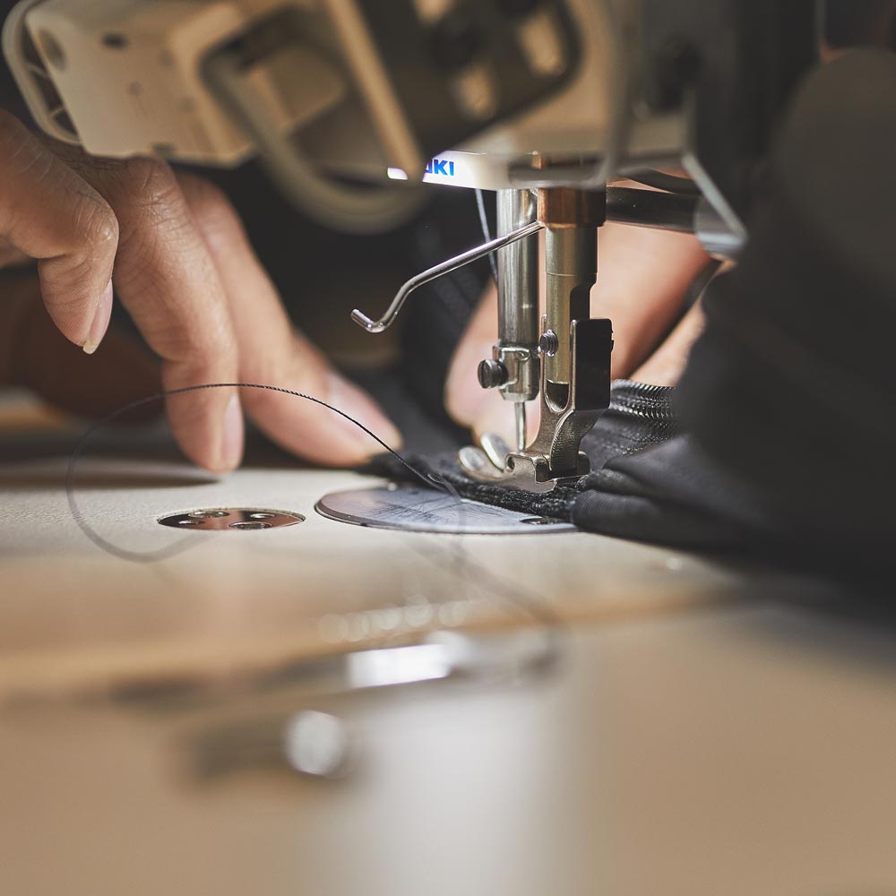 Close-up of hands using a sewing machine to stitch black fabric with a needle and thread.