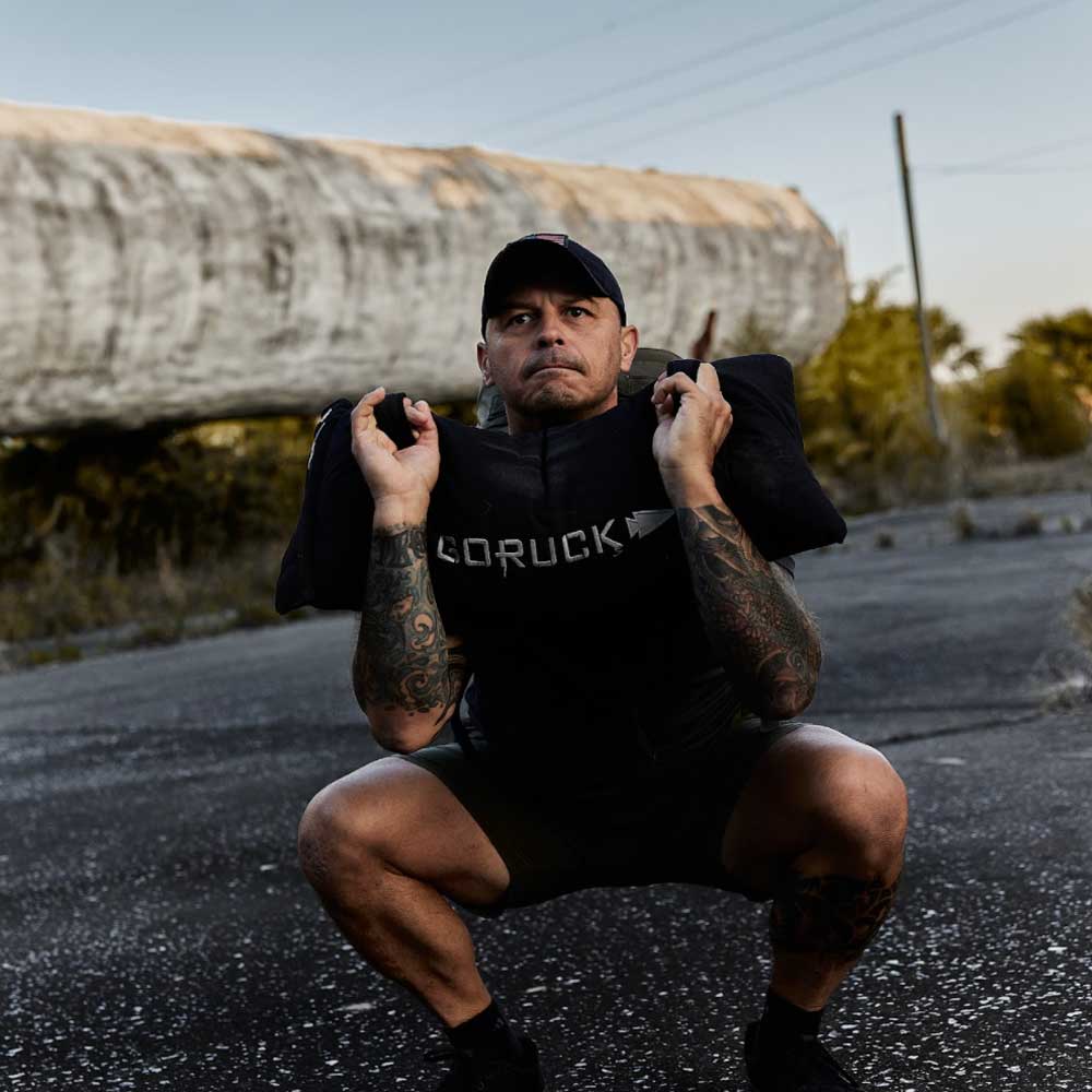 A man squatting with a large log behind him.
