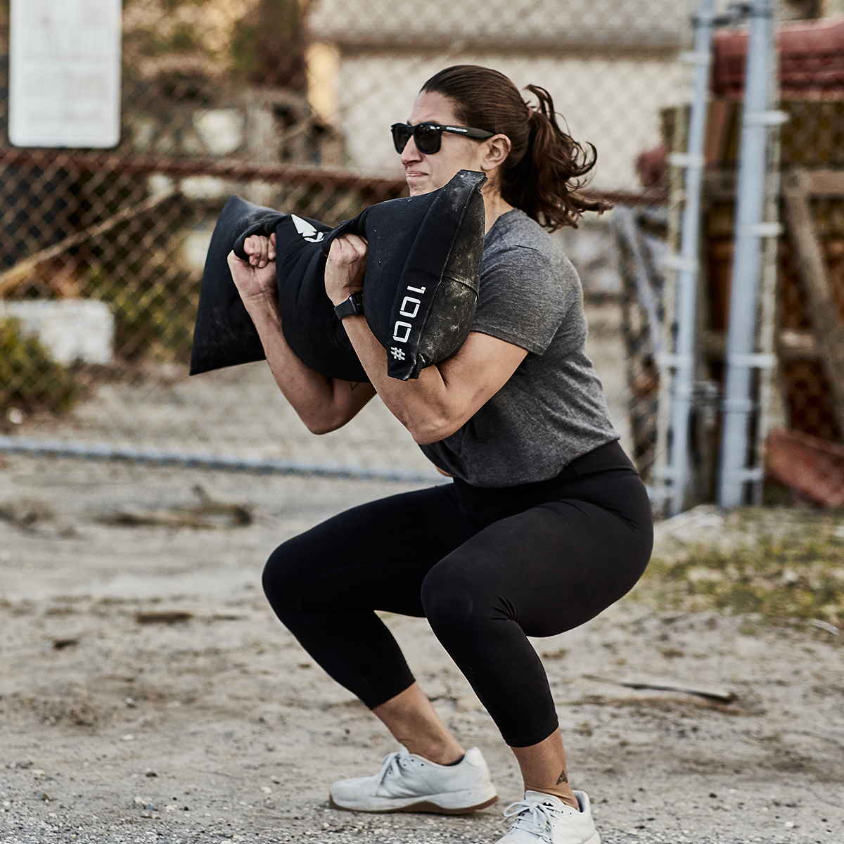 Woman performing outdoor squat with GORUCK 100 lb ruck sandbag, fitness gear