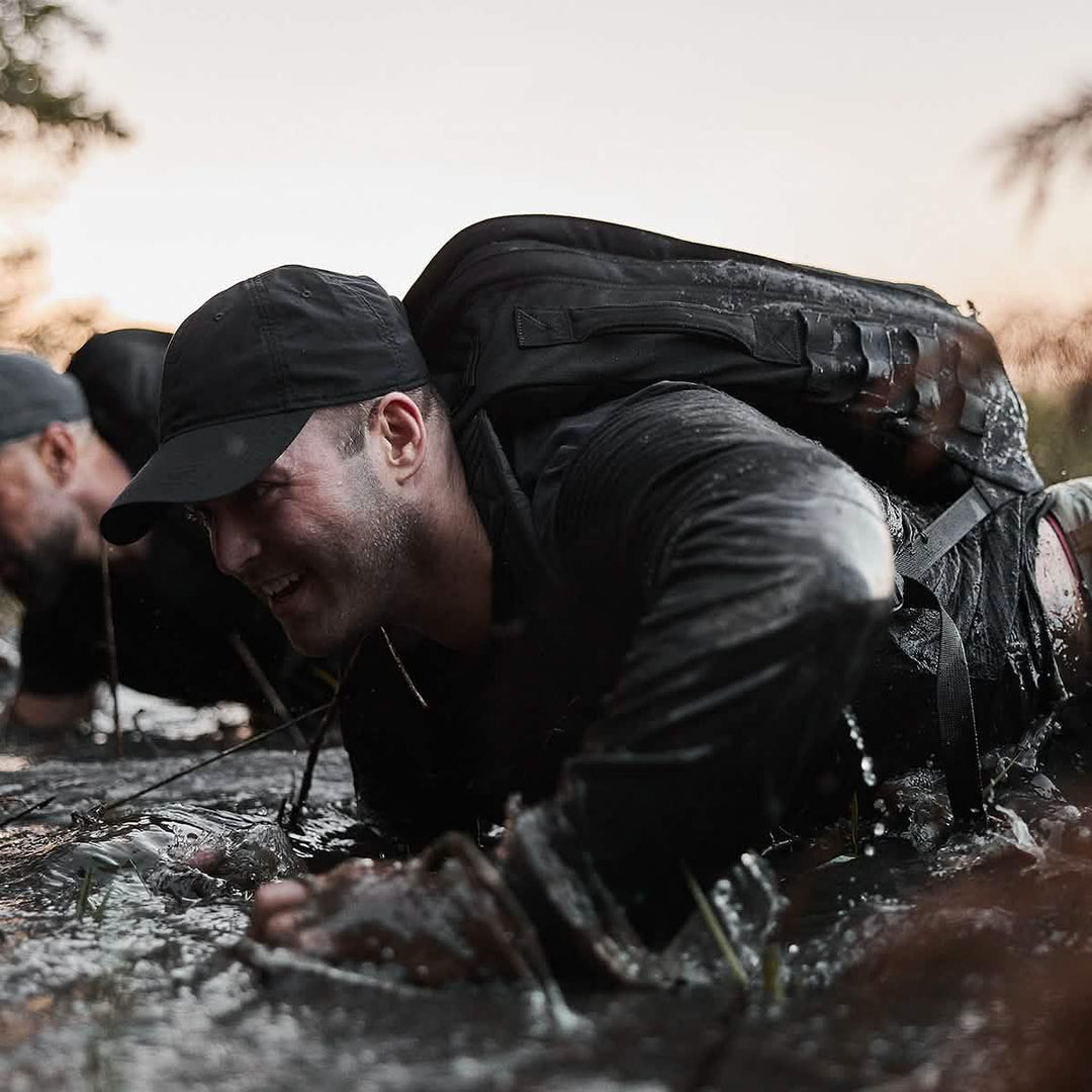 Man wearing GORUCK hat and backpack crawling through mud during intense ruck training