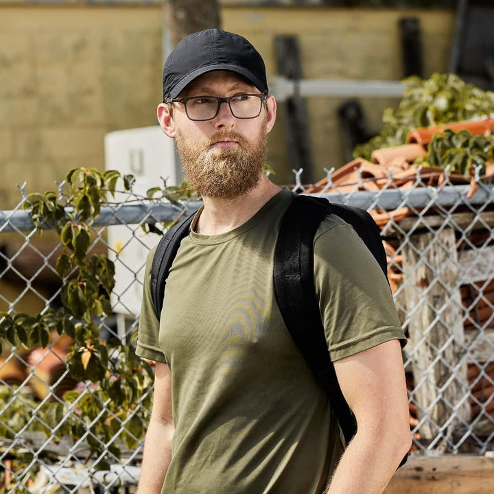 Man wearing black GORUCK hat, olive green shirt, and black backpack outdoors