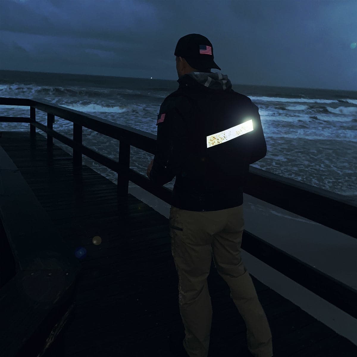 Wearing the Speed Rucker, a person strolls on a dark, windy boardwalk by the ocean at night.