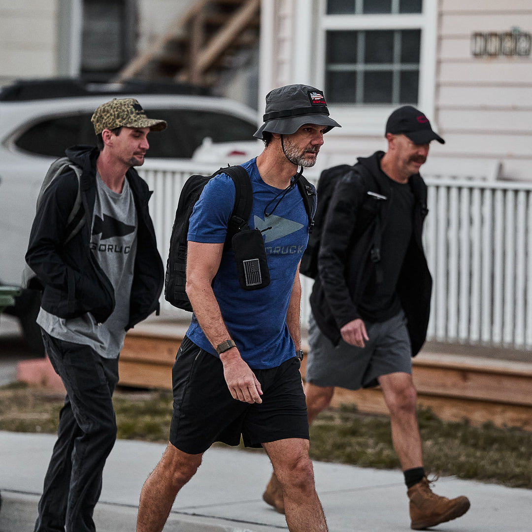 Three men wearing vendor-unknown’s Three Rules Tee - Tri-Blend walk outdoors in casual style hats by a house and white fence, as if posing for photos.