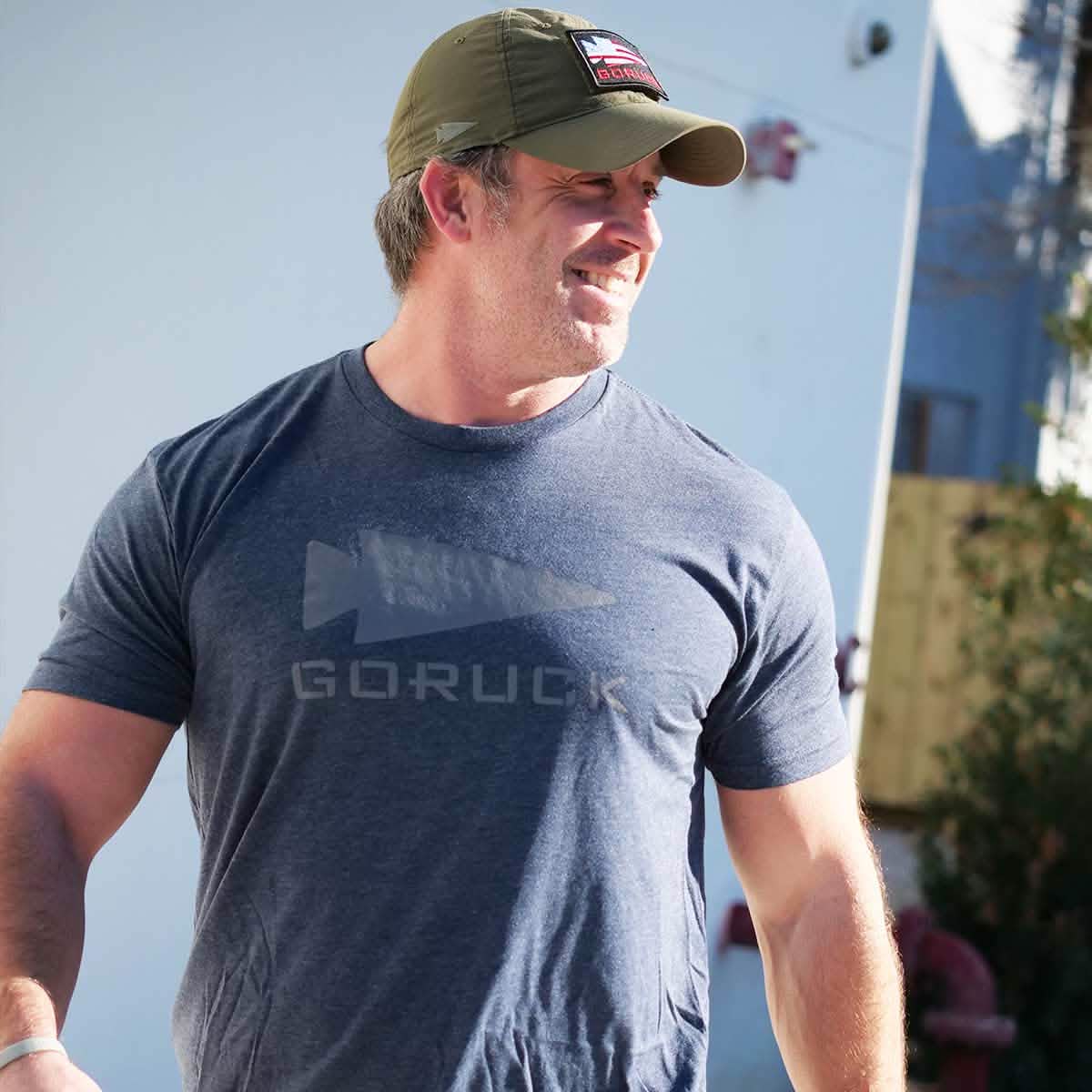 A man in a green cap and the Three Rules Tee - Tri-Blend from vendor-unknown stands outdoors, smiling in the sunlight, ready for semi-famous photos.