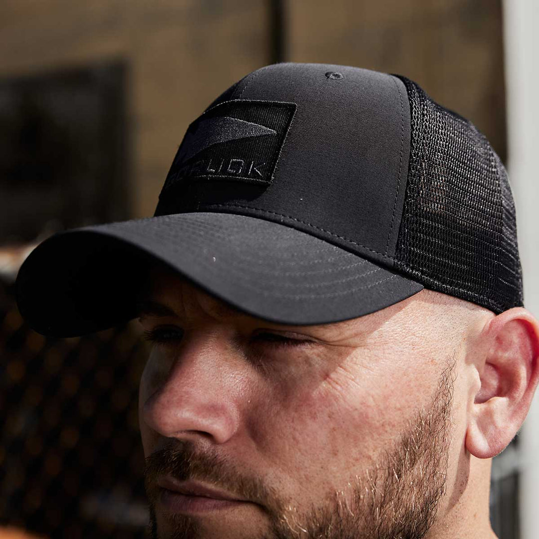 A man outdoors is wearing the GORUCK Performance Trucker Hat - GORUCK Spearhead, featuring mesh sides and an adjustable Velcro strap for a perfect fit.