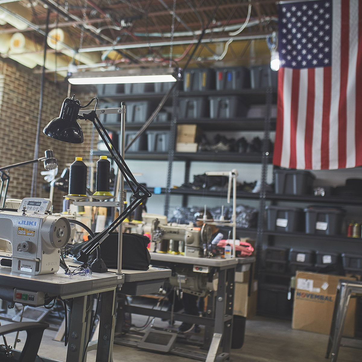 A sewing workshop with sewing machines, shelves of storage bins, and a large American flag on the wall.