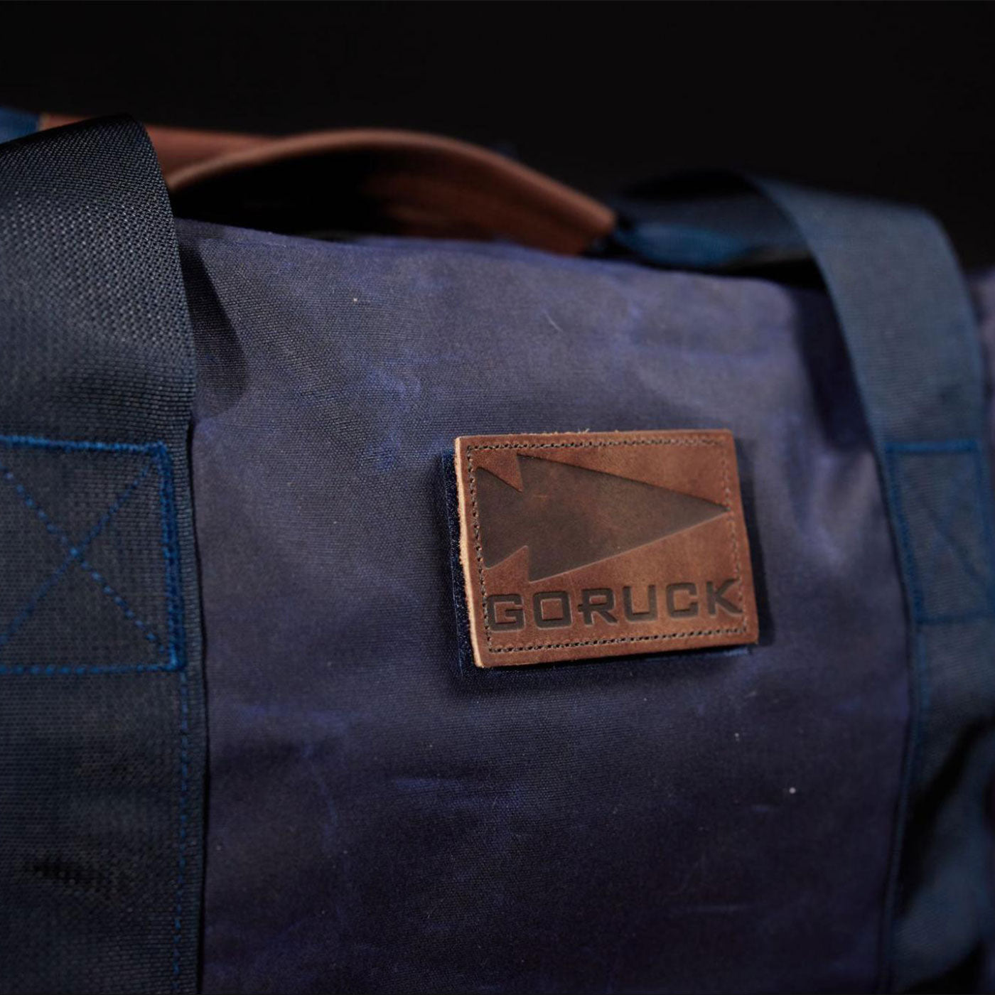 Close-up of a navy blue duffel bag with a brown leather GORUCK logo patch.