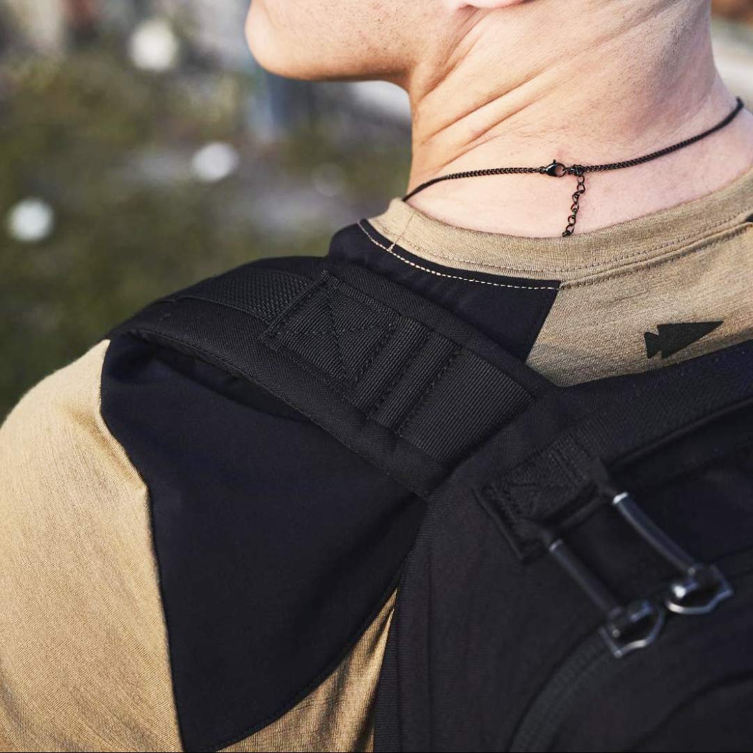 Close-up of a person wearing a black backpack and a black necklace, seen from behind and slightly to the side.